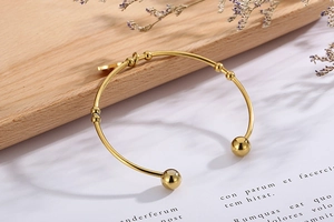 Detail of golden stainless steel open cuff bracelet with spherical ends on wooden tray