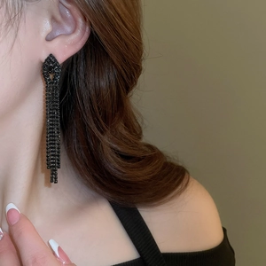 Detail shot of long dark tassel earrings with sparkling rhinestones on model's ear