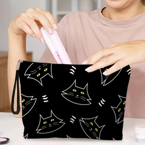 Portable black cat print makeup bag with yellow eyes and metal zipper being held by hand