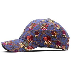 Detail of blue canvas baseball cap featuring colorful cartoon owl prints and curved brim