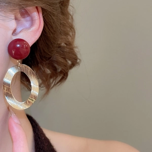 Close-up of brushed metal oval earrings with a red resin bead on female model ear