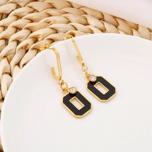 Macro detail of geometric black and gold earrings with white crystal on a ceramic plate