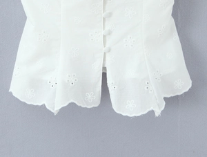 Detailed view of white floral eyelet embroidery blouse with scalloped hem and fabric buttons