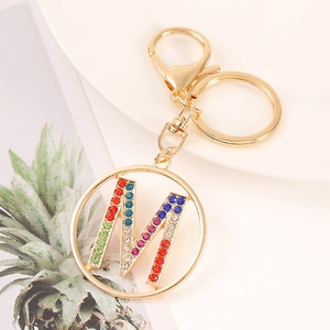 Close-up of golden letter M keychain pendant with multi-colored crystals on a tray