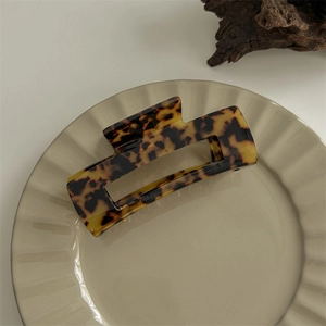 Close-up of a large leopard print acetate claw clip on a beige decorative ceramic tray