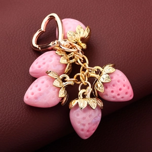 Close-up of pink resin strawberry charms with golden metal leaves on red leather