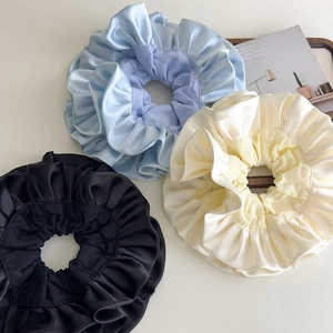 Three oversized satin scrunchies in blue, beige, and black with elegant pleated textures