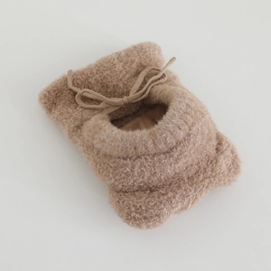 Detail of plush brown baby booties with soft fleece texture and ribbon bow decoration