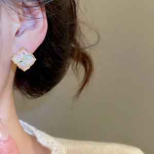 Detail showing elegant gold-rimmed enamel rhombus earring worn on a female model