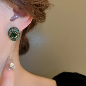 Close-up of vintage emerald stud earrings with green rhinestones and antique gold finish