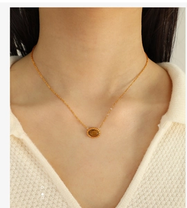 Close-up of golden necklace with oval tiger eye pendant and twisted texture on model