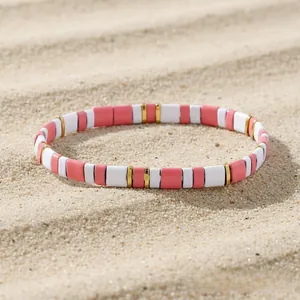 Detail of pink and gold Tila bead bracelet laying on white sand with soft shadows