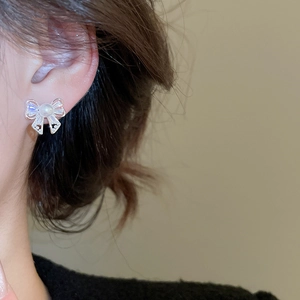 Detail of bow-shaped earring with white pearl and sparkling rectangular zircons on model