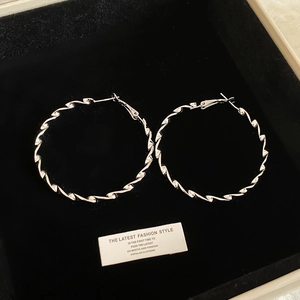Macro detail of large silver-colored twisted geometric hoop earrings on black velvet