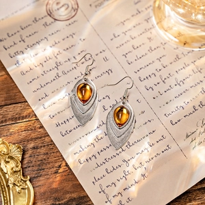 Detailed view of vintage silver earrings with amber teardrop gems on retro letter paper