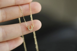 Detailed close-up of a 14K gold plated silver U-shaped horseshoe pendant with small diamonds