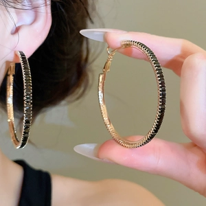 Macro shot of large gold hoop earrings with black zircon stones worn by a female model