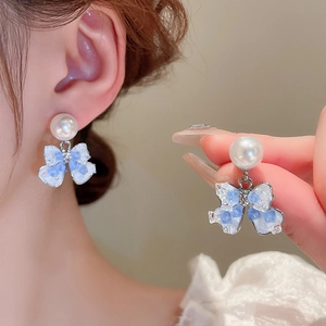 Elegant pearl bow earrings with blue stone resin charm shown in a worn and close-up view