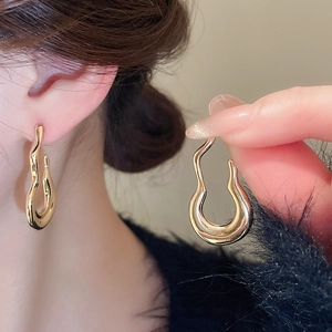 Detail of elegant gold irregular wave hoop earrings shown worn and held in hand