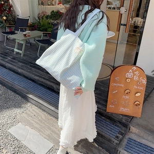 Detail view of the green striped canvas tote bag with side label in outdoor street setting
