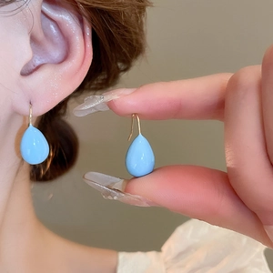 Close-up of blue water drop enamel earrings with gold hooks on model's ear