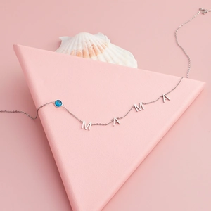 Detail of silver MAMA letter necklace featuring a small round blue gemstone pendant
