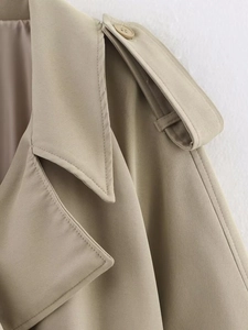 Detail of khaki trench coat featuring buttoned shoulder epaulets and a wide lapel collar
