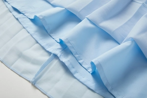 Gros plan sur l'ourlet de la robe plissée bleu clair montrant la couture et la texture mousseline