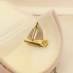 Detailed close-up of a golden sailboat brooch with pavé zircon stones in a velvet box