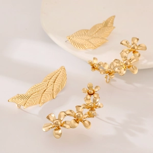 Minimalistische goudkleurige blad en bloem ear cuff set op witte keramische schaal