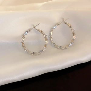 Close-up of silver geometric faceted hoop earrings on elegant white silk fabric