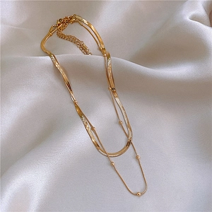 Detail of double-layer golden stainless steel snake chain and beaded necklace on silk