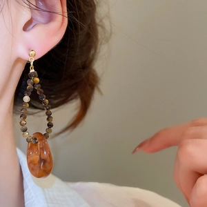 Détail de boucles d'oreilles dorées avec perles œil de tigre et pendentif en résine