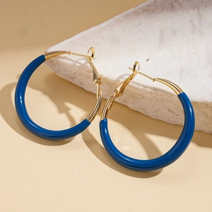 Close-up of klein blue enamel and gold geometric hoop earrings on marble texture