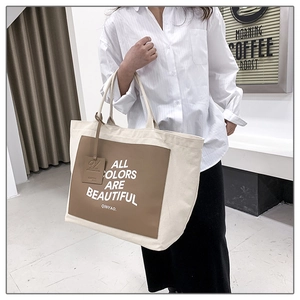Detail view of large canvas tote bag with brown leather patch and printed text slogan