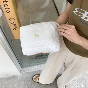 Close-up of white quilted cosmetic bag with heart patterns and gold logo label