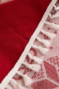 Macro shot of red Christmas reindeer tablecloth with white fringe detail and jacquard texture