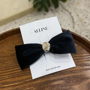 Detail of black velvet bow hair clip with gold metal center on a white display card