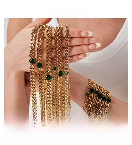 Detail view of layered gold Cuban link bracelets and necklaces with emerald gemstones