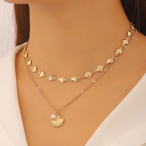 Dettaglio di una collana dorata a due strati con ciondoli a stella marina, conchiglia e perla