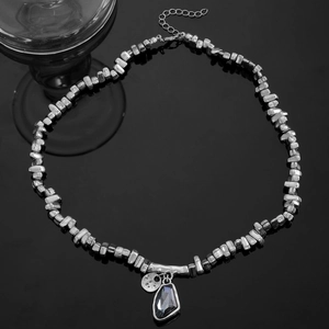 Détail du collier perles argentées avec pendentif goutte sombre sur fond noir miroir