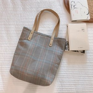 Macro view of plaid canvas tote with leather handles on a white textured bedsheet