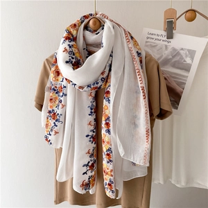 Close-up of white sun protection scarf with colorful floral embroidery on a wooden hanger