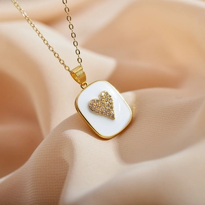 Macro shot of white enamel square pendant with a sparkling gold heart on silk