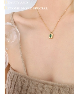 Close-up of a model wearing a gold chain necklace with a rectangular green gemstone pendant