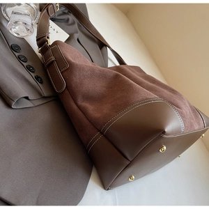 Detail of brown faux suede tote bag with white stitching and protective metal feet