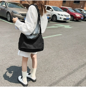 Outdoor shot of a black oversized canvas messenger bag worn by a person from behind
