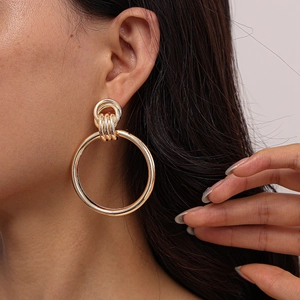 Close-up of a model wearing large golden geometric hoop earrings with a polished finish