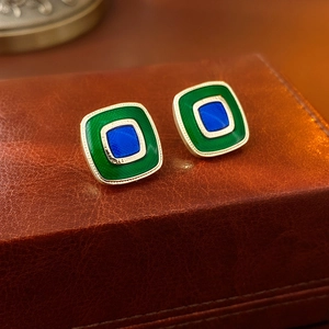 Macro shot of vintage gold square earrings with blue and green enamel on leather