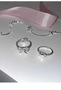 Macro shot of silver bow and heart beaded rings with necklace on white surface